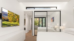 Una habitación de hotel moderna con una cama grande, un televisor y un balcón con vistas a árboles.