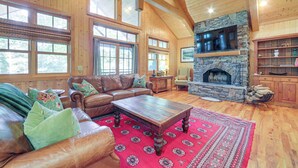 A spacious living room with a stone fireplace, leather furniture, and large windows. - Scenic Mtn & Fairway Views: Cozy Cashiers Getaway (Cashiers)