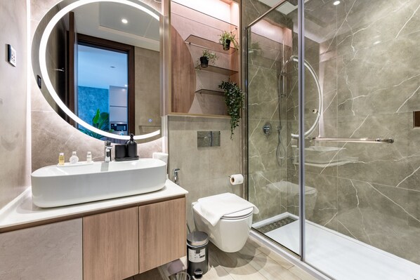 A modern bathroom with a large mirror, a sink, a toilet, and a glass-enclosed shower.