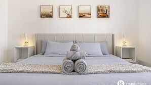 Une chambre à coucher avec un lit, deux tables de chevet avec des lampes, un tapis et trois tableaux encadrés accrochés au mur.