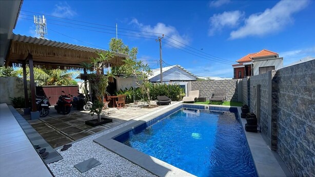 A swimming pool with a stone wall, a covered seating area, and a parked motorcycle. - Pradnya Homestay - 1Bedroom Near Uluwatu (Ungasan)