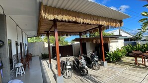 A covered outdoor area with a thatched roof, two motorcycles parked, and a table with chairs. - Pradnya Homestay - 1Bedroom Near Uluwatu (Ungasan)