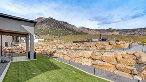 Un edificio moderno con un patio cubierto, un césped cuidado y un paisaje rocoso al fondo.