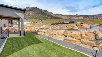 A modern building with a covered patio area, a well-maintained lawn, and a rocky landscape in the background.
