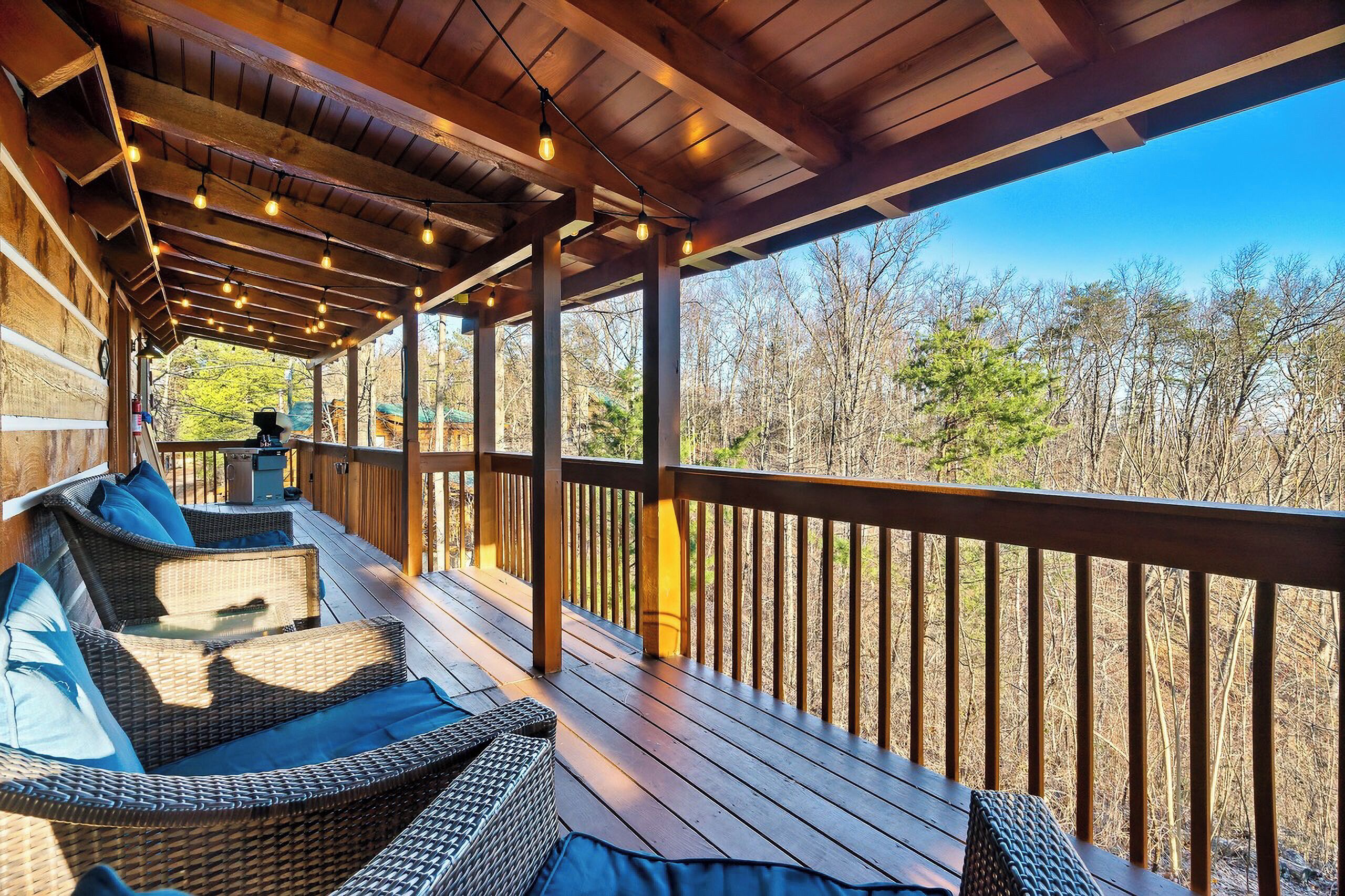 A covered outdoor deck with wicker furniture and a railing, overlooking a forested area.