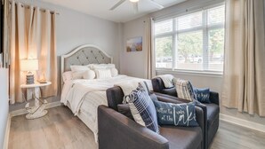 Une chambre à coucher avec un lit, un ventilateur de plafond, une fenêtre avec des rideaux et une table de chevet avec une lampe.