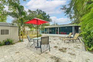 Un espace patio avec une table et des chaises, un parasol rouge et un coin salon abrité.