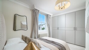 Een slaapkamer met een bed, een bedlamp, een raam met gordijnen, een spiegel en een kledingkast.