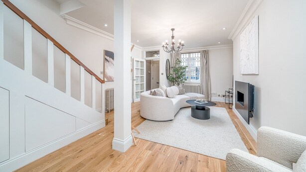 Een ruime woonkamer met een gebogen witte bank, een ronde salontafel en een open haard. Een trap met houten leuningen leidt naar een hoger gelegen niveau.