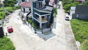 A multi-story residential building with a balcony, a gated driveway, and a red car parked on the street. - Room-luxurious Double Deluxe With Wifi n (Lucena)
