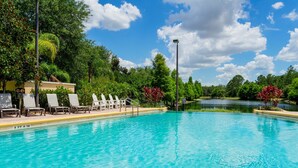 A clear blue pool with lounge chairs and a small bridge.