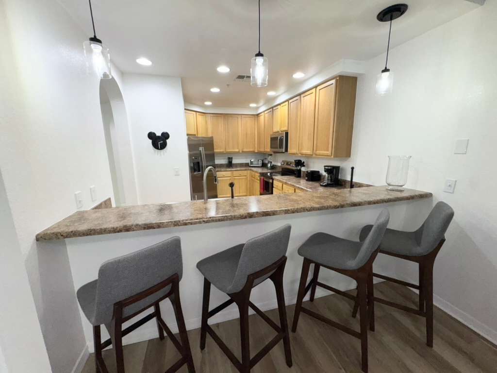 Una cocina moderna con armarios de madera, encimera de granito y tres taburetes de bar.