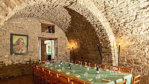 A dining area with a stone wall, wooden chairs, a long table with green tablecloths, and candles.