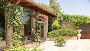 A stone building with a wooden pergola entrance, a glass door, and a stone wall with greenery.