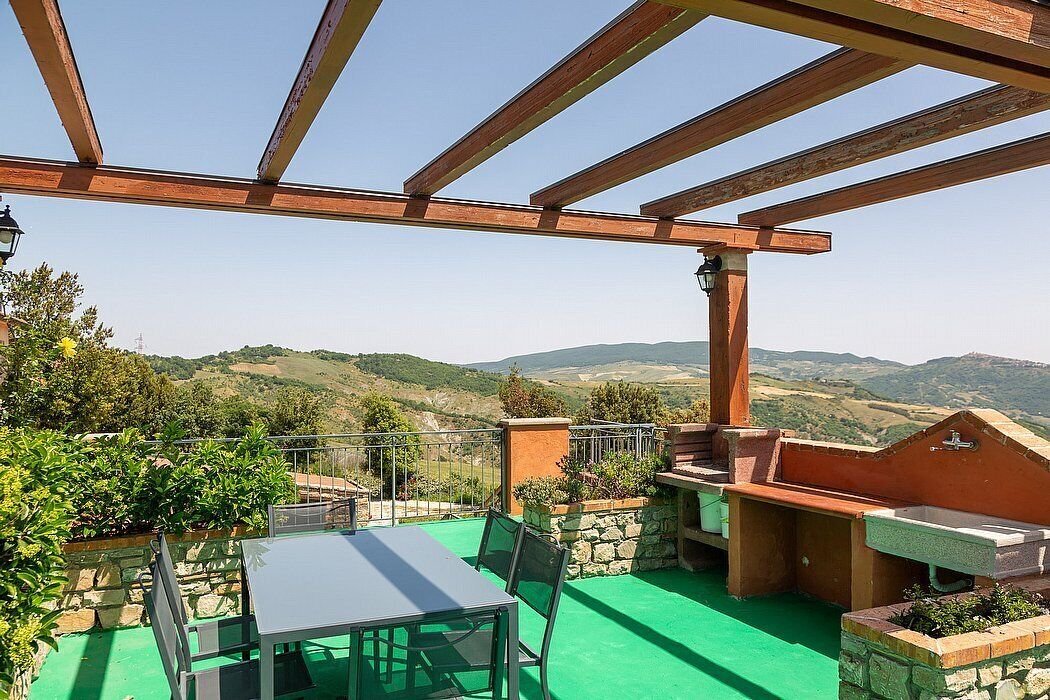 A patio with a table and chairs, a barbecue area, and a view of rolling hills.