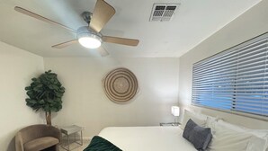 A bedroom with a bed, a ceiling fan, a wall-mounted air vent, a window with blinds, a small round rug, a potted plant, and a chair. - Old Town Scottsdale / 4 Bedroom House (Scottsdale)