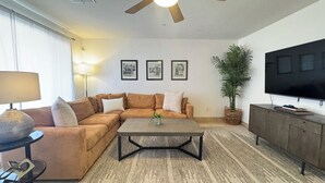 A living room with a sectional sofa, a coffee table, a TV on a cabinet, and a ceiling fan. - Old Town Scottsdale / 4 Bedroom House (Scottsdale)