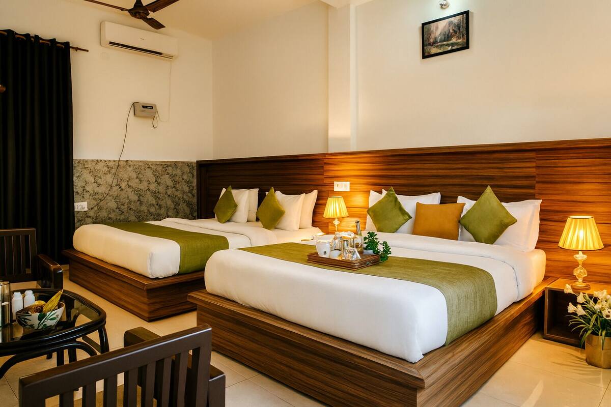 A hotel room with two beds, a wooden headboard, a small table with a tray of toiletries, and a wall-mounted air conditioner.