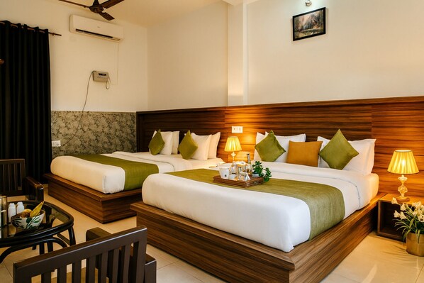 A hotel room with two beds, a wooden headboard, a small table with a tray of toiletries, and a wall-mounted air conditioner.