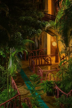Un jardín tropical interior con una escalera de madera, abundante follaje y una fuente de agua.