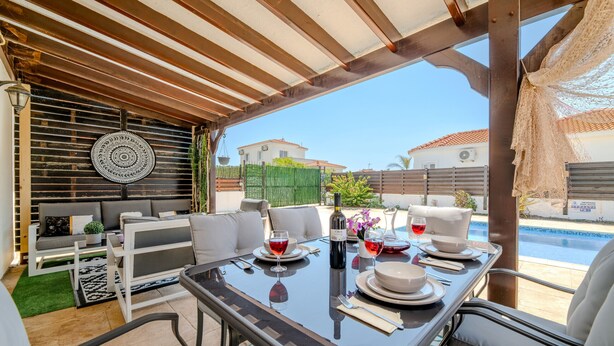 Un patio al aire libre con una mesa de comedor para dos, un sofá y una piscina al fondo.