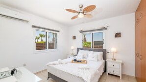 Un dormitorio con cama, mesitas de noche, ventilador de techo y ventanas con persianas.