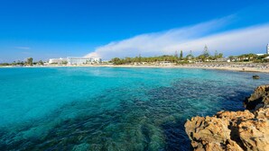 Ein Küstenhotel mit klarem, blauem Wasser, felsiger Küstenlinie und einem Strand mit Sonnenschirmen.