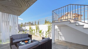 Ein Terrassenbereich im Freien mit Korbmöbeln, einer Treppe und Blick auf ein Gebäude im Hintergrund.