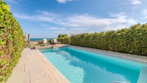 Une piscine rectangulaire à l’eau d’un bleu limpide, entourée d’une haie basse et d’une terrasse carrelée.