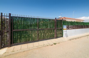 A gated area with a metal fence, a white wall, and a building with a red roof in the background. - Sunrise Ayia Thekla Bungalow (Sotira)