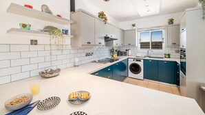 Een moderne keuken met witte en blauwe kastjes, een ingebouwde wasmachine en een ontbijtarrangement met ontbijsgerechten en gebak.