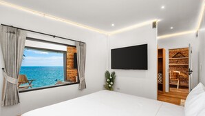 Un dormitorio con una cama grande, un televisor montado en la pared, una ventana con cortinas y vistas al océano.