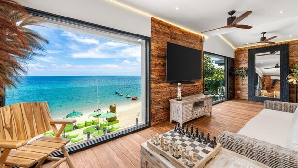 Un salón amplio con un gran ventanal con vistas a la playa, una chimenea y un tablero de ajedrez.