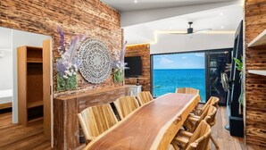 Un comedor moderno con una mesa y sillas de madera, un adorno en la pared y vista al océano.