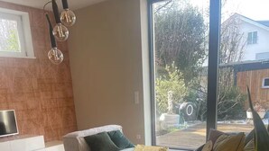 A modern living room with a large window, a sofa set, and a flat-screen TV on a white console.
