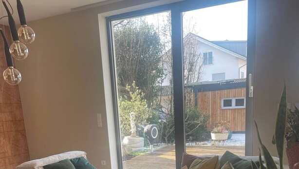 A modern living room with a sofa, a coffee table, and a laptop. There is a large window providing a view of the outside.