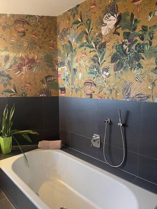 A bathroom with a bathtub, a shower, and a floral-patterned wall.