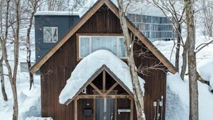 Una cabaña de madera con techo a dos aguas, rodeada de árboles cubiertos de nieve.