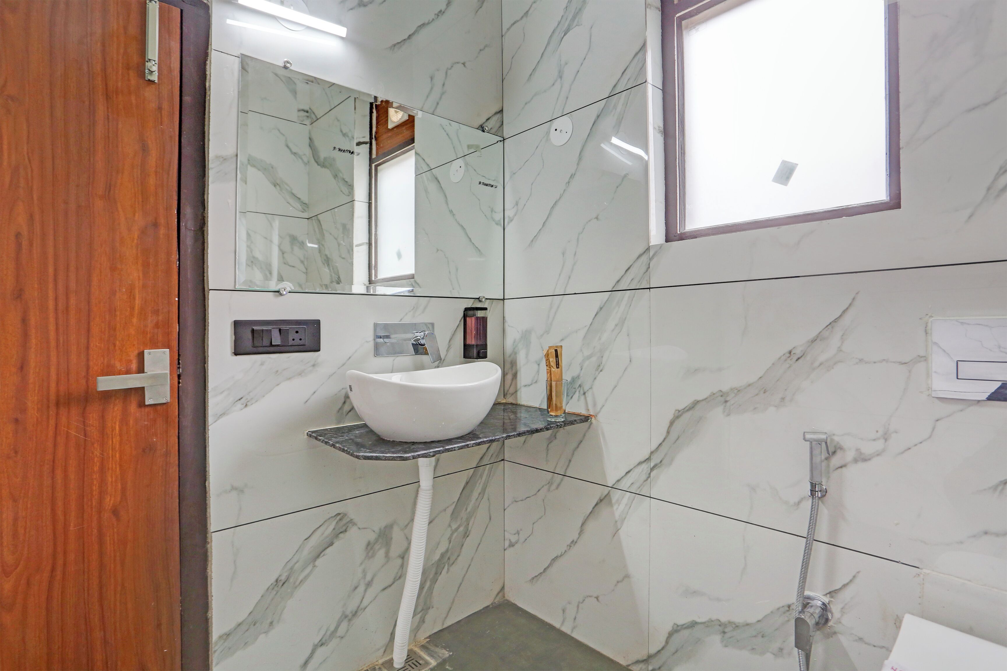 A bathroom with a marble wall, a white sink, a mirror, and a shower.