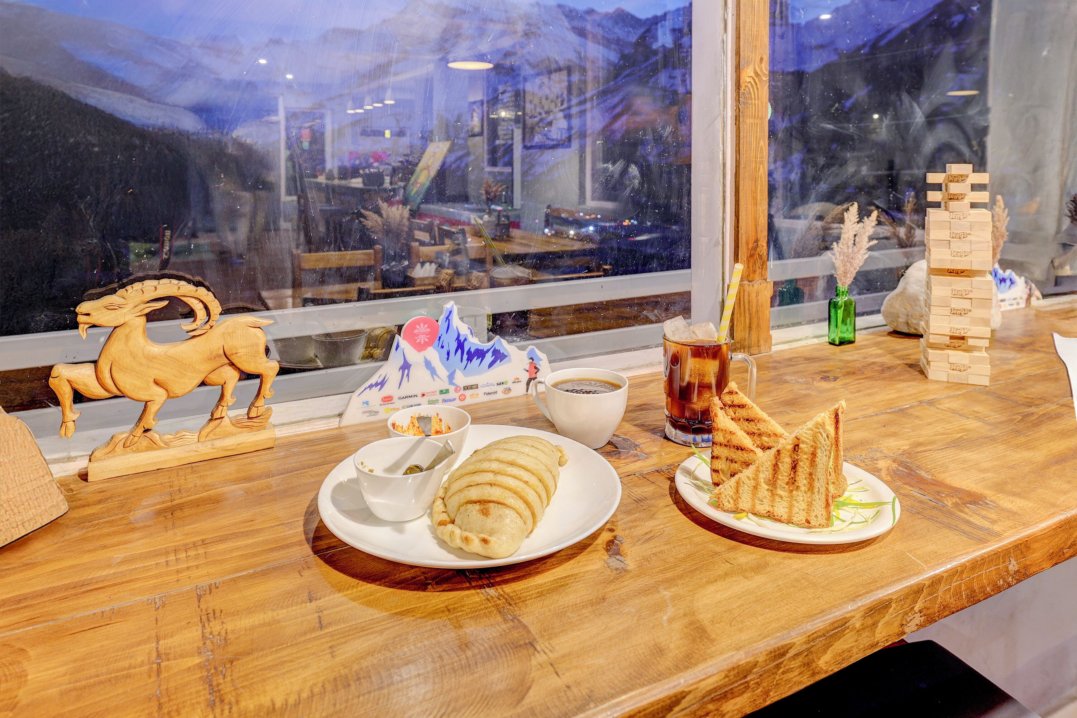 Una mesa de madera con un plato de comida, una taza de café y un caballo de madera decorativo.