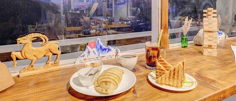 Una mesa de madera con un plato de comida, una taza de café y un caballo de madera decorativo.