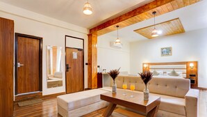 A modern living room with a wooden floor, a sofa, a coffee table, and a dining table. There are two pendant lights hanging from the ceiling. - Utpala House By Lifestyle (Lahul)