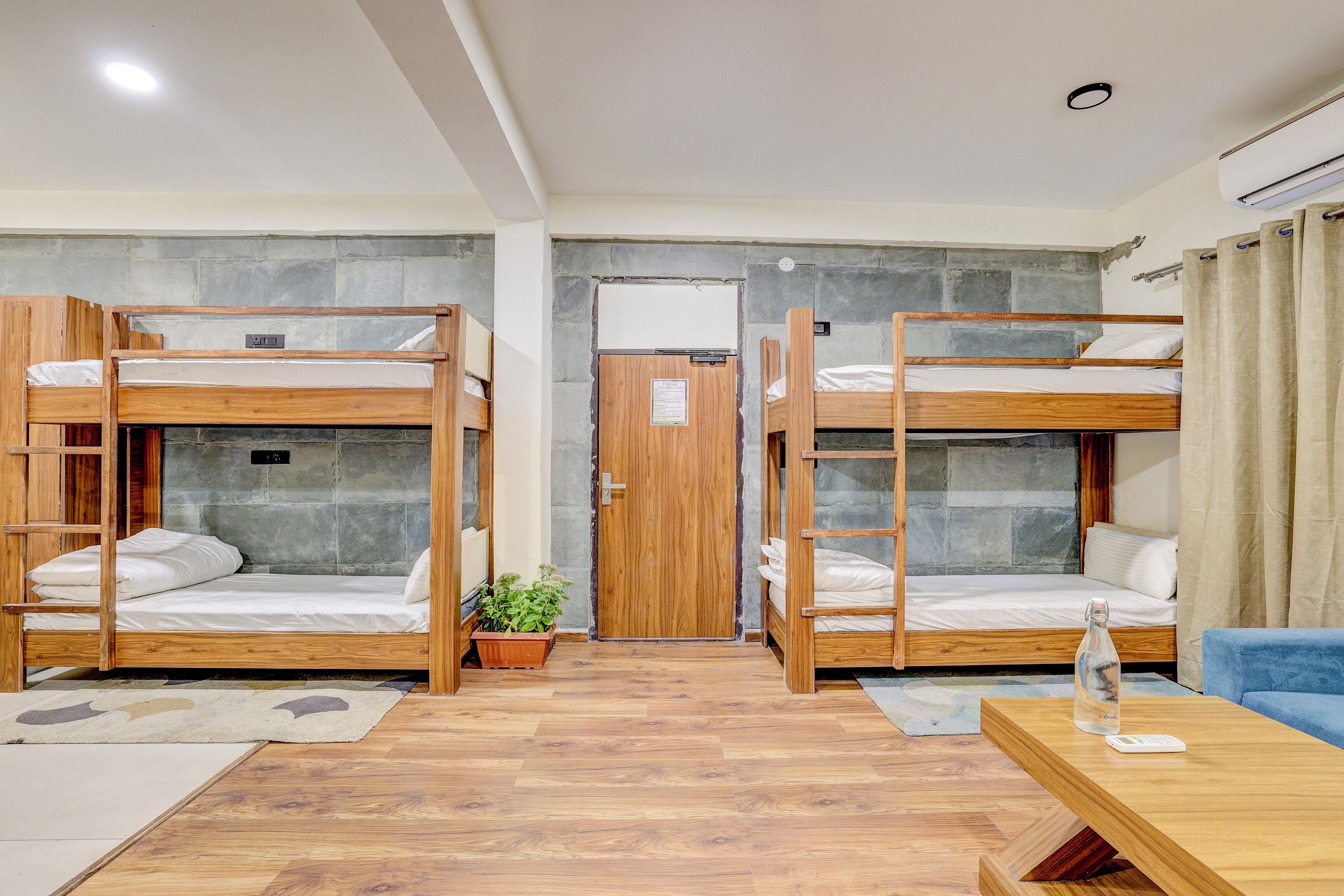 A room with bunk beds, a wooden table, a potted plant, and a door with a sign.