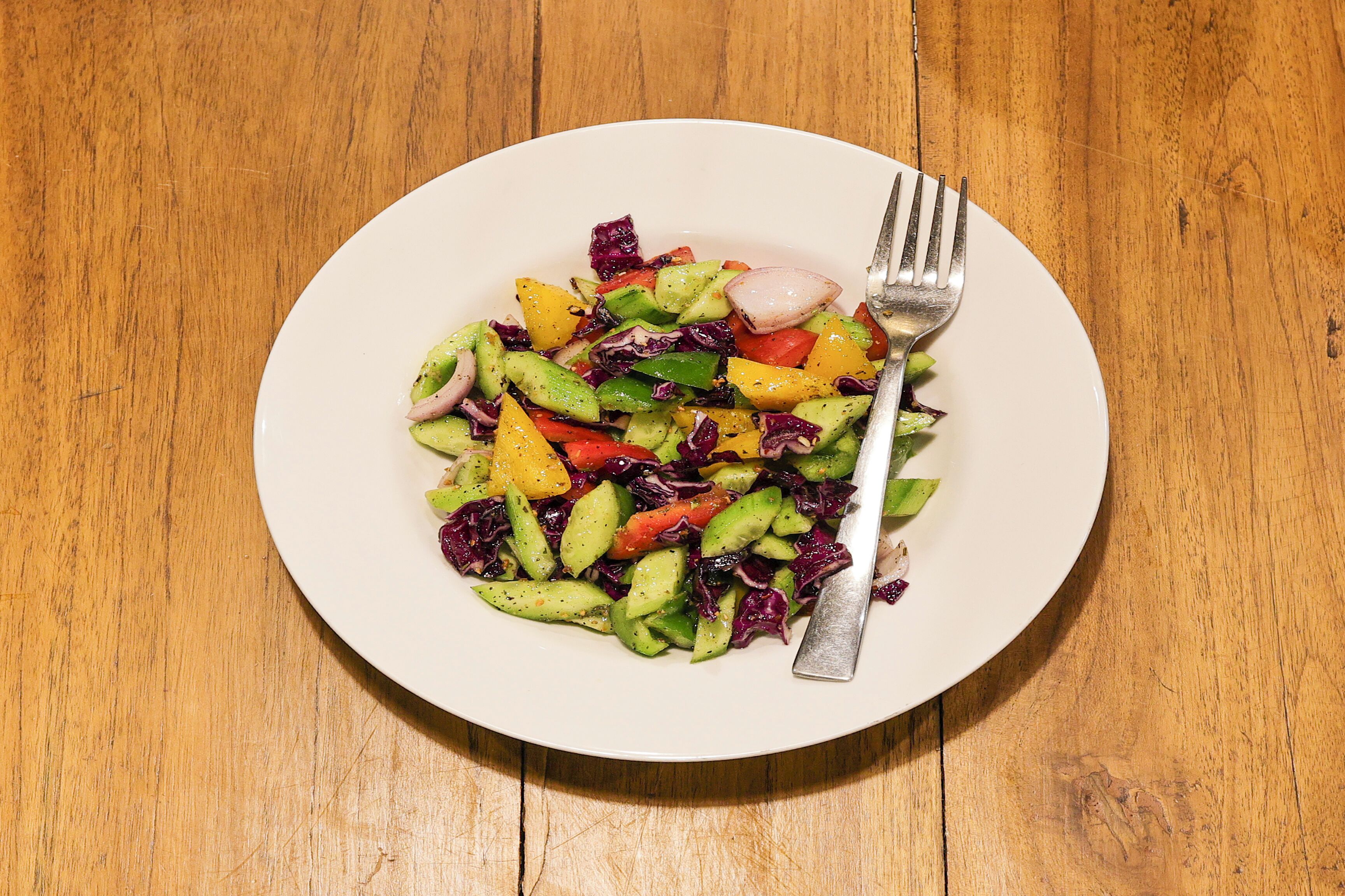 Un plato blanco con una ensalada de verduras coloridas sobre una mesa de madera.