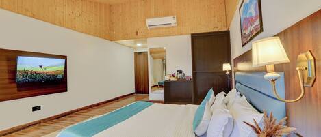 A spacious bedroom with a large bed, wooden ceiling, a flat-screen TV, a bedside table with a lamp, and a mirror.