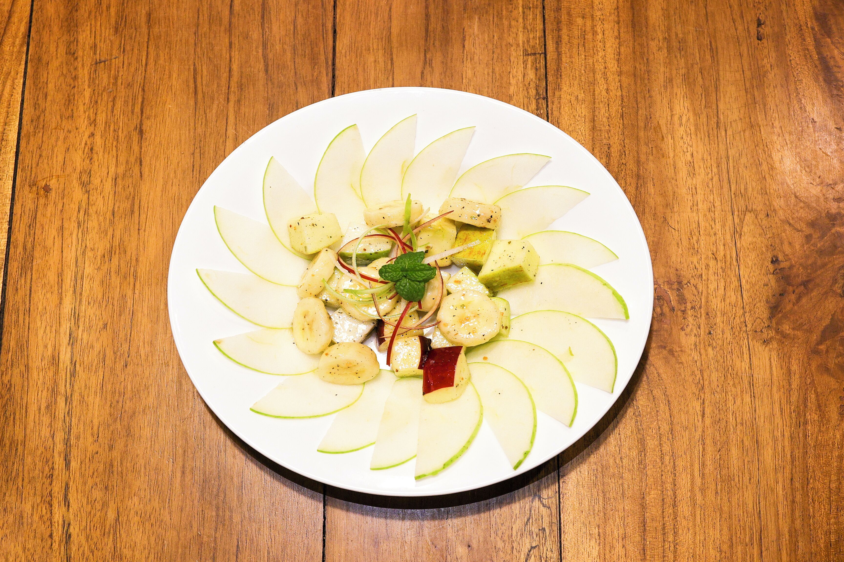 A plate of sliced apples arranged in a circular pattern on a wooden table.