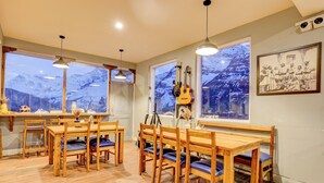 A dining area with wooden furniture, large windows with mountain views, and a framed picture on the wall. - Utpala House By Lifestyle (Lahul)