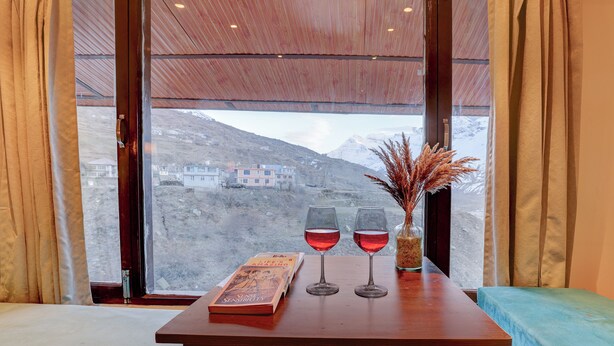 A room with a wooden table, two glasses of red wine, a book, and a vase with dried plants. - Utpala House By Lifestyle (Lahul)