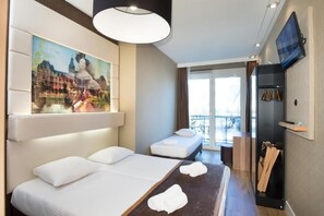Une chambre d’hôtel avec un grand lit, un lit plus petit, un tableau, une télévision et un balcon avec vue.