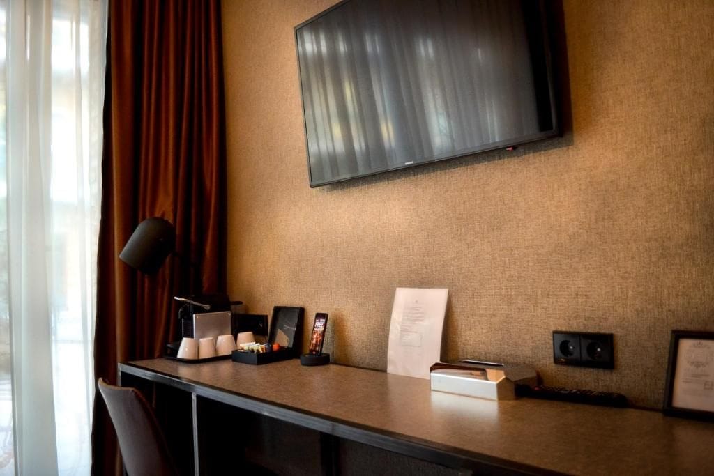 Habitación de hotel con televisor de pantalla plana montado en la pared, un escritorio con lámpara, teléfono y un cuadro enmarcado.